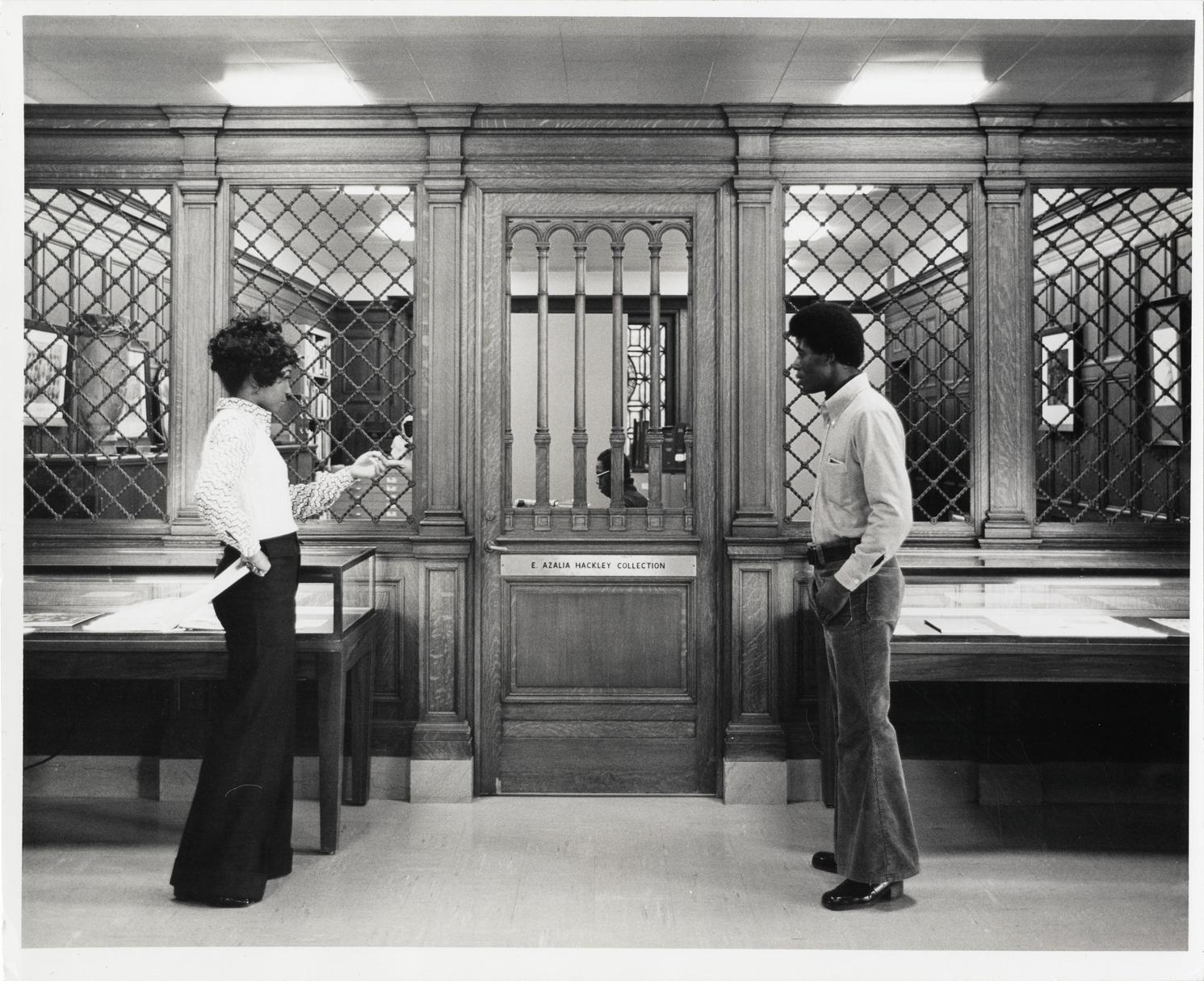 Woman and man stand in front of the E. Azalia Hackley Collection at the Detroit Public Library.